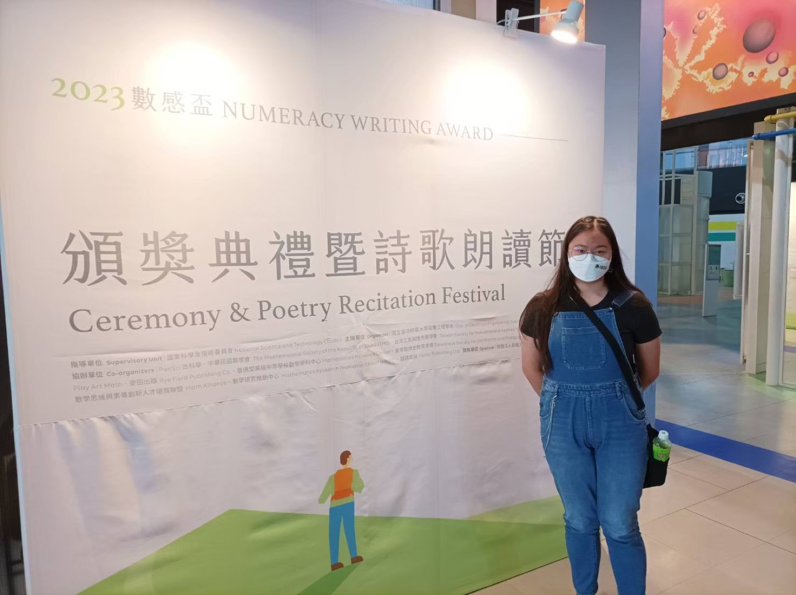 In front of the Numeracy Writing Award Ceremony & Poetry Recitation Festival banner